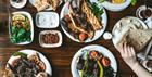 Plates of colourful middle-eastern vegetable and meat dishes set out on a wooden table with salads and dips