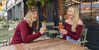 Two women sharing a laugh with colourful cocktails in Flight Club's flowery summer terrace