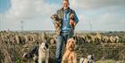 Adam Henson holding 2 dogs, surrounded by dogs