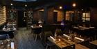 Wooden tables set with cutlery, napkins and wine glasses in a dark-painted and wood-panelled restaurant with soft lighting