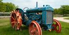 A blue vintage Fordson tractor with faded red wheels sits on a grassy patch at Cotswold Farm Park