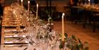 A long table is set with candles, cutlery, glassware and foliage in a warm evening light.