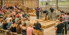 A crowd of families sit in a barn watching an interesting demonstration of sheep shearing. A Cotswold Farm Park employee is presenting in the centre w