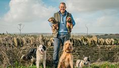 Adam Henson holding 2 dogs, surrounded by dogs