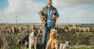 Adam Henson holding 2 dogs, surrounded by dogs