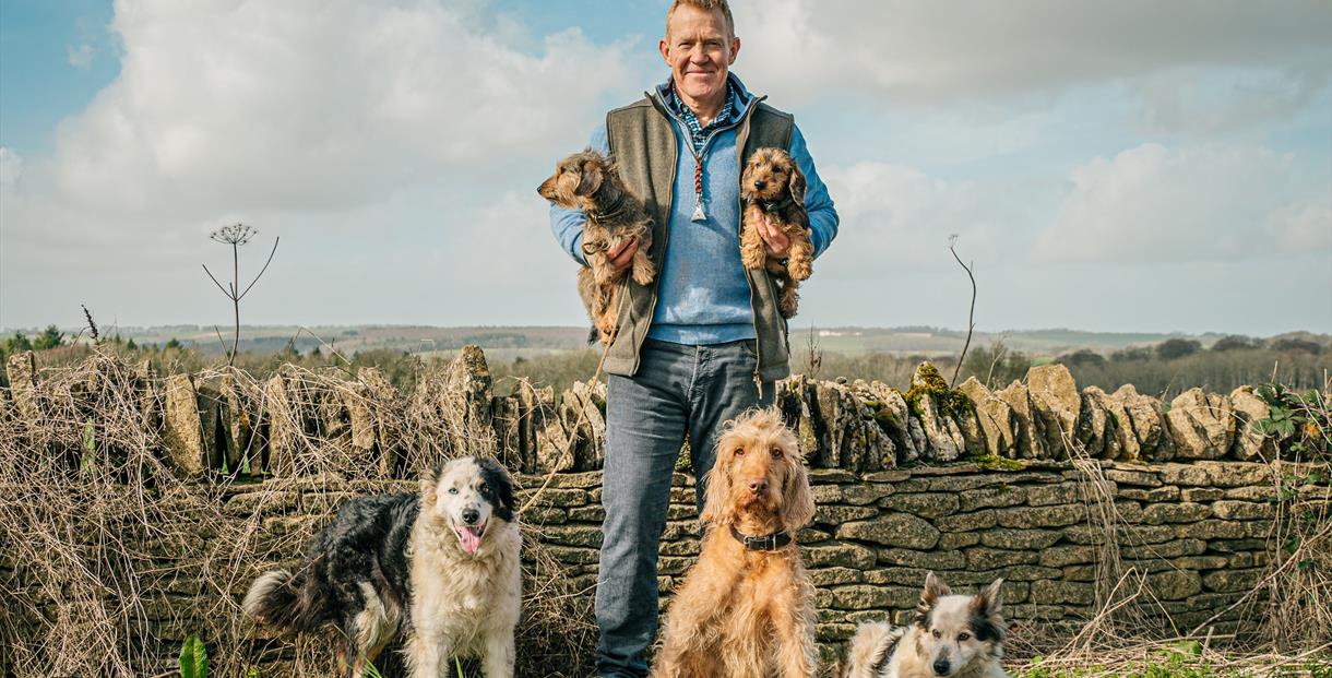 Adam Henson holding 2 dogs, surrounded by dogs