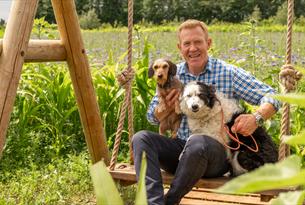 Adam Henson sat on a swing holding two dogs