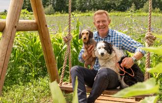 Adam Henson sat on a swing holding two dogs