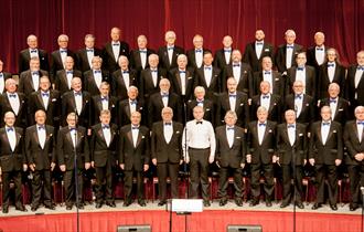 The Gentlemen Songsters Male Voice Choir in uniform on stage.