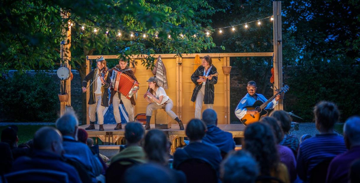 Small outdoor theatre stage lit up in the night with 5 performers playing music