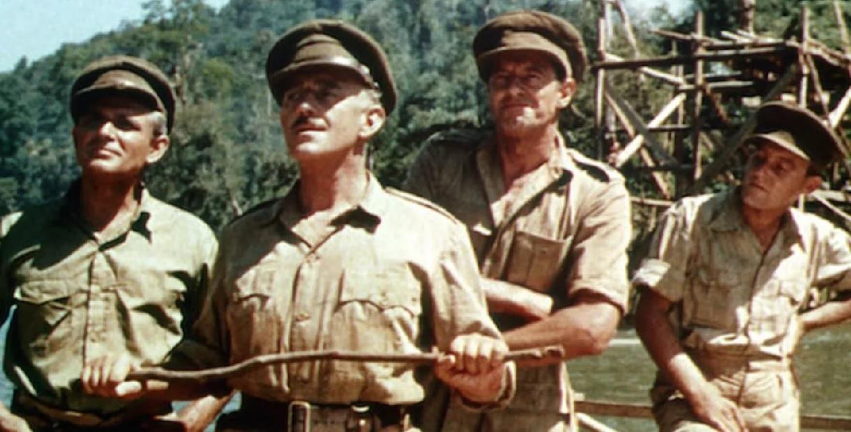 Alec Guiness as Colonel Nicholson with three other soldiers standing on the bridge