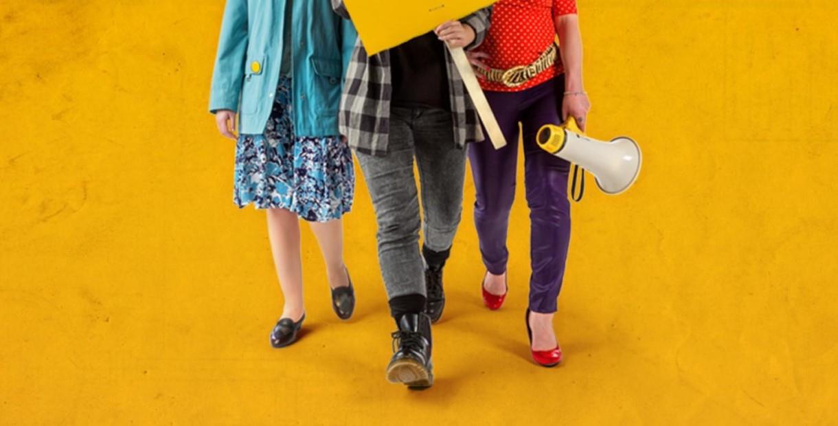 The legs of three women who are holding a sign and megaphone