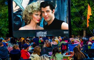 Grease film playing on outdoor cinema screen with crowds watching