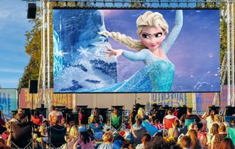 Frozen film playing on outdoor cinema screen with crowds watching