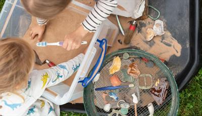 Two young girls playing in a sandpit looking for archaeological finds with a toothbrush and trowel