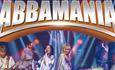 The female band members are centre stage singing while the other band members are to either side of them playing instruments, with the title Abbamania
