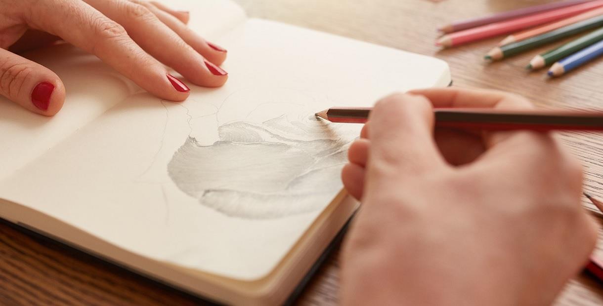 A woman's hands shading in a sketchbook with a pencil