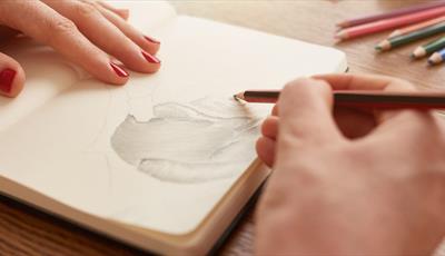 A woman's hands shading in a sketchbook with a pencil