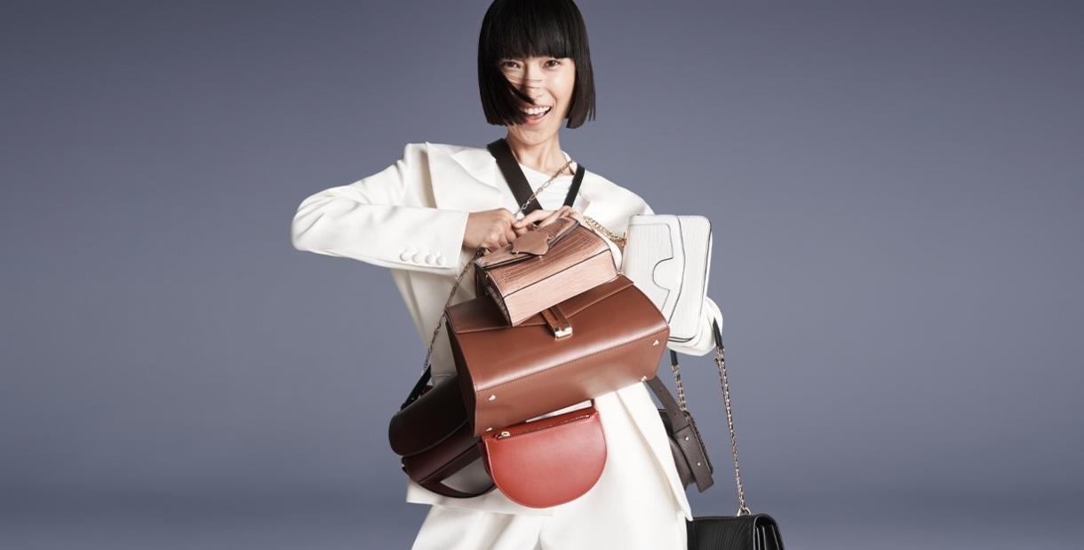 Lady smiling holding lots of designer handbags