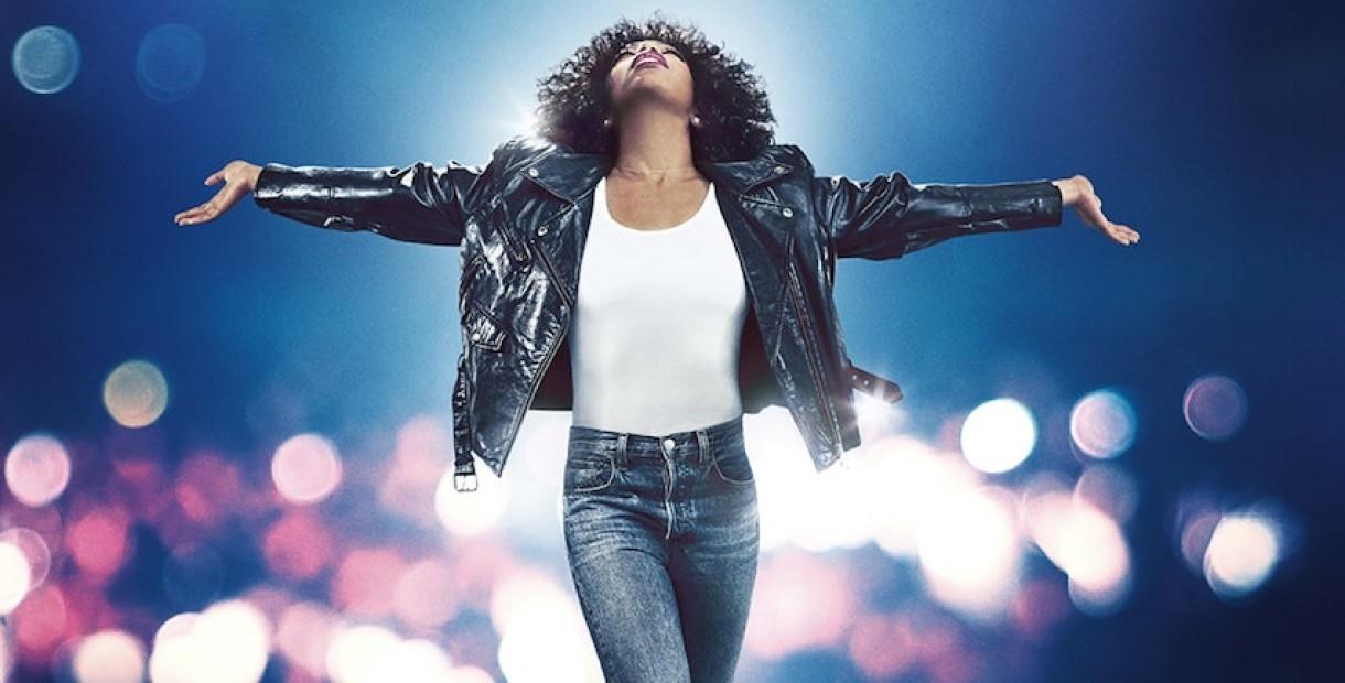 Naomi Ackie as Whitney Houston in jeans and a denim jacket looking up with her arms out