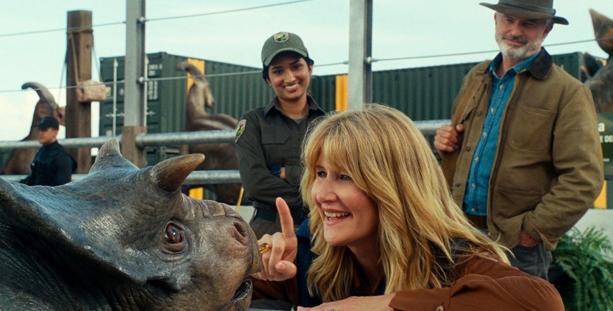 Laura Dern smiling at a baby Dinosaur with Sam Neill watching on from the background