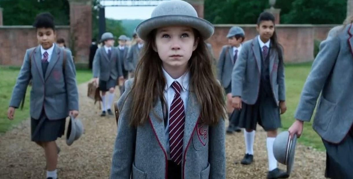 Matilda in a grey hat and school uniform walking through school gates with other children
