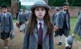 Matilda in a grey hat and school uniform walking through school gates with other children