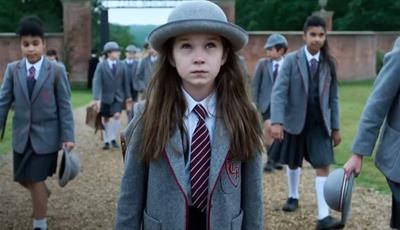 Matilda in a grey hat and school uniform walking through school gates with other children 