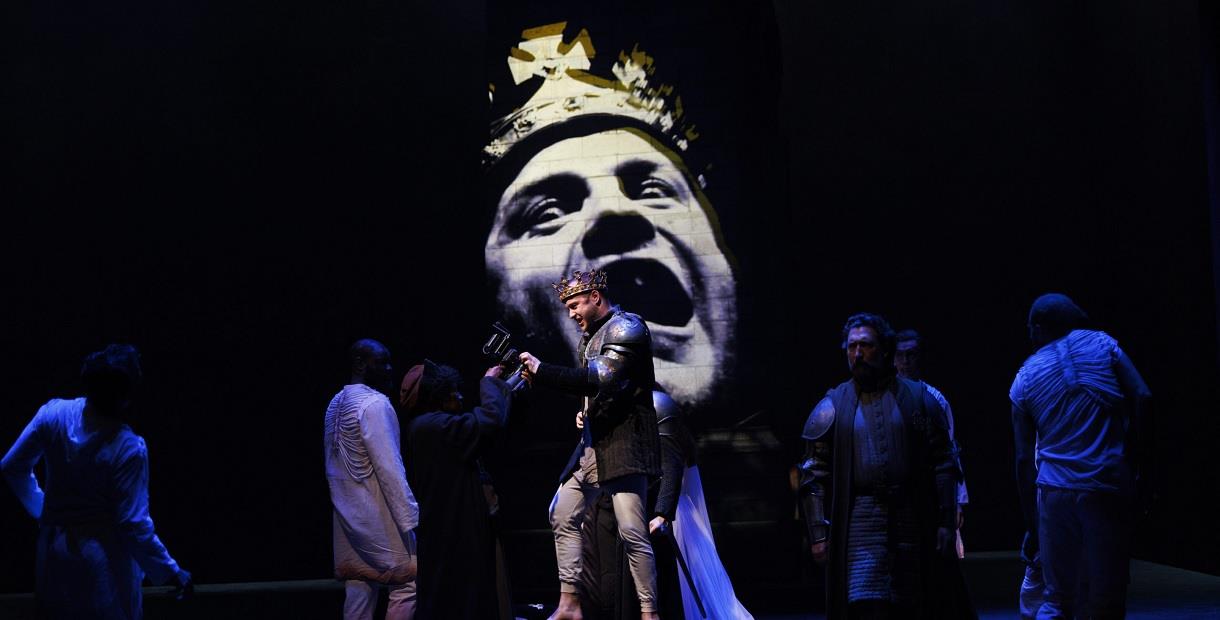 Actors in the foreground as the face of Richard the third looms large on a screen behind.