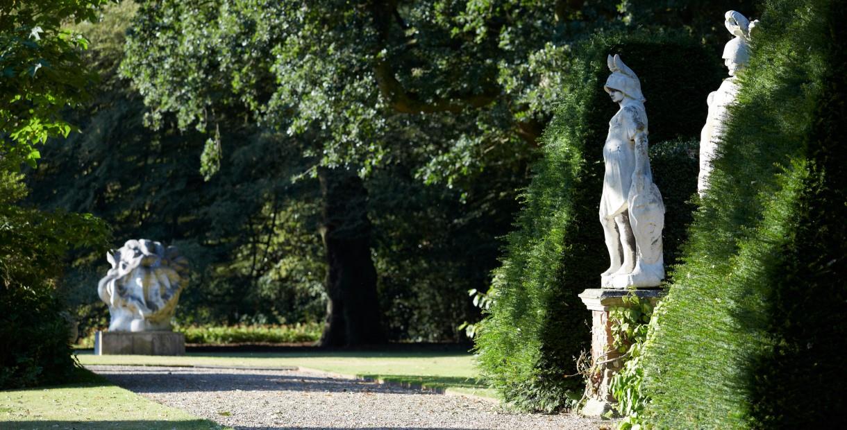 Three statues and manicured hedges with a gravel path running through the middle