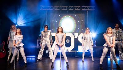 The seven members of Stage Theatre Productions performing on stage in white and silver costumes 