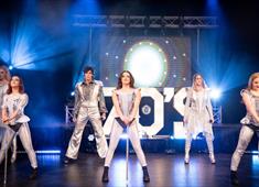 The seven members of Stage Theatre Productions performing on stage in white and silver costumes