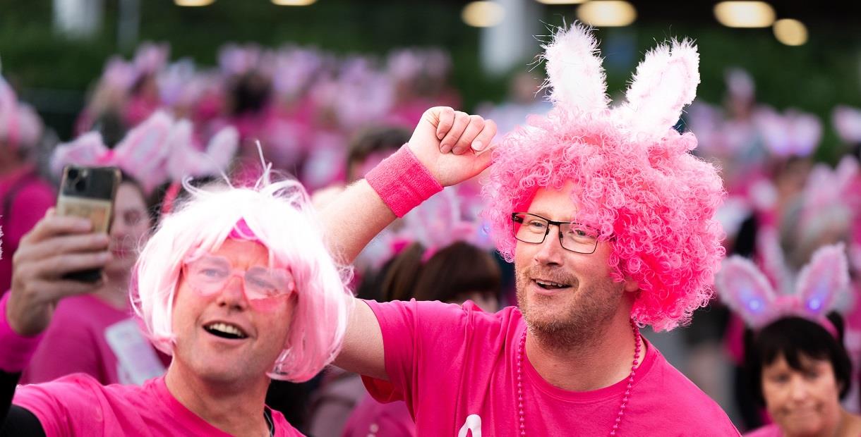 Two men in pink wigs and t-shirts smiling