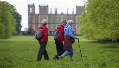 Three walkers strolling through the grounds with Hardwick Hall in the background