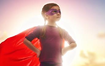 Girl in a super hero costume with red cape and pink mask
