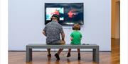 A father and son watch a video installation