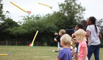 5 children of different ages throw brightly coloured foam arrows in a field