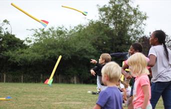 5 children of different ages throw brightly coloured foam arrows in a field