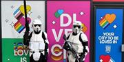 Two storm troopers stand in front of brightly coloured hordings
