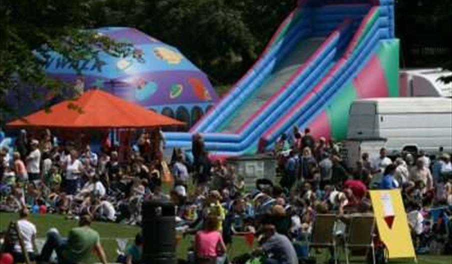 Large crowd of people enjoying the sunshine, with a bouncy castle and inflatables behind them.