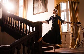 A ballet dancer, dressed as florence nightingale, dances on a grand wooden staircase.