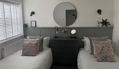 Twin bedroom with pink and green cushions on bed