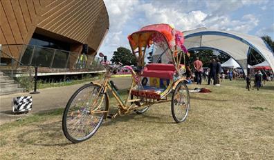 A colourful rickshaw/tricycle stands in front of firstsite - a large golden curved building.