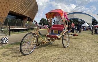 A colourful rickshaw/tricycle stands in front of firstsite - a large golden curved building.