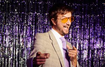 Man in yellow glasses with a purple glitter backdrop