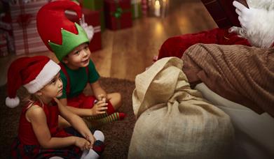 Two children in elf costumes sit at Santa's feet.