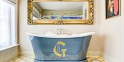 Blue roll top bath with gold letter G motif
