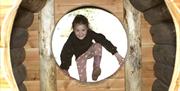 Girl climbing through wooden hole on a climbing frame