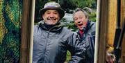 Bob and Paul stand in wet weather gear in front of a river