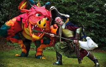 A comically dressed pirate  brushed the teeth of an oversized friendly dragon with a customised hobby horse